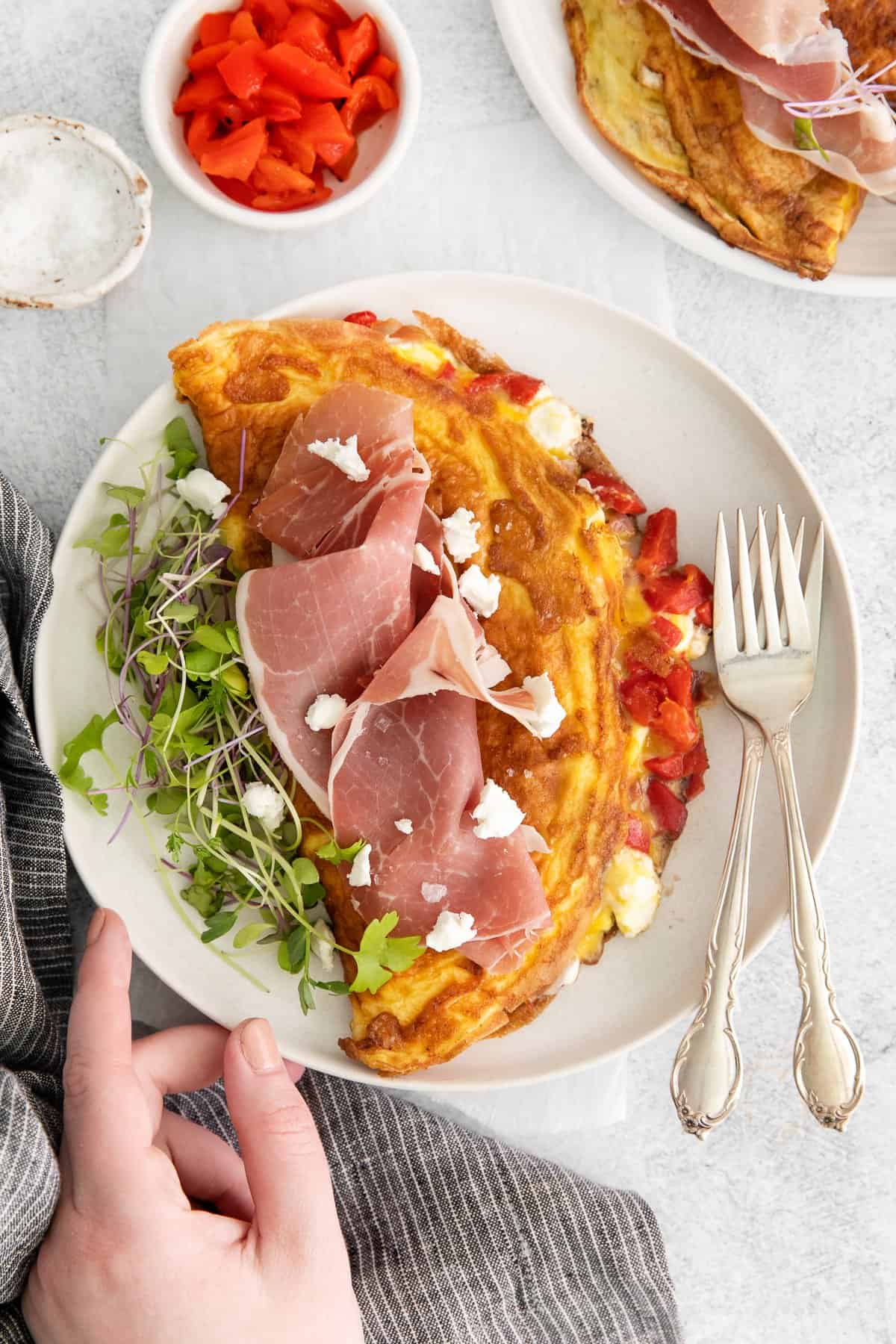 Goat cheese omelet on a plate that is topped with prosciutto and micro greens. 