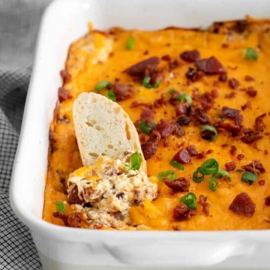 a crostini being dipped into Cheddar Bacon Cream Cheese Dip