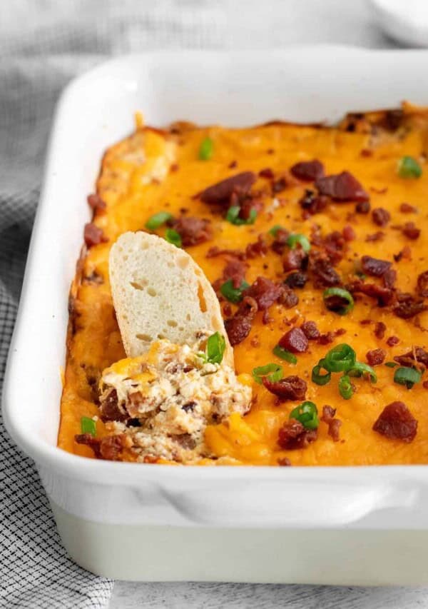 a crostini being dipped into Cheddar Bacon Cream Cheese Dip