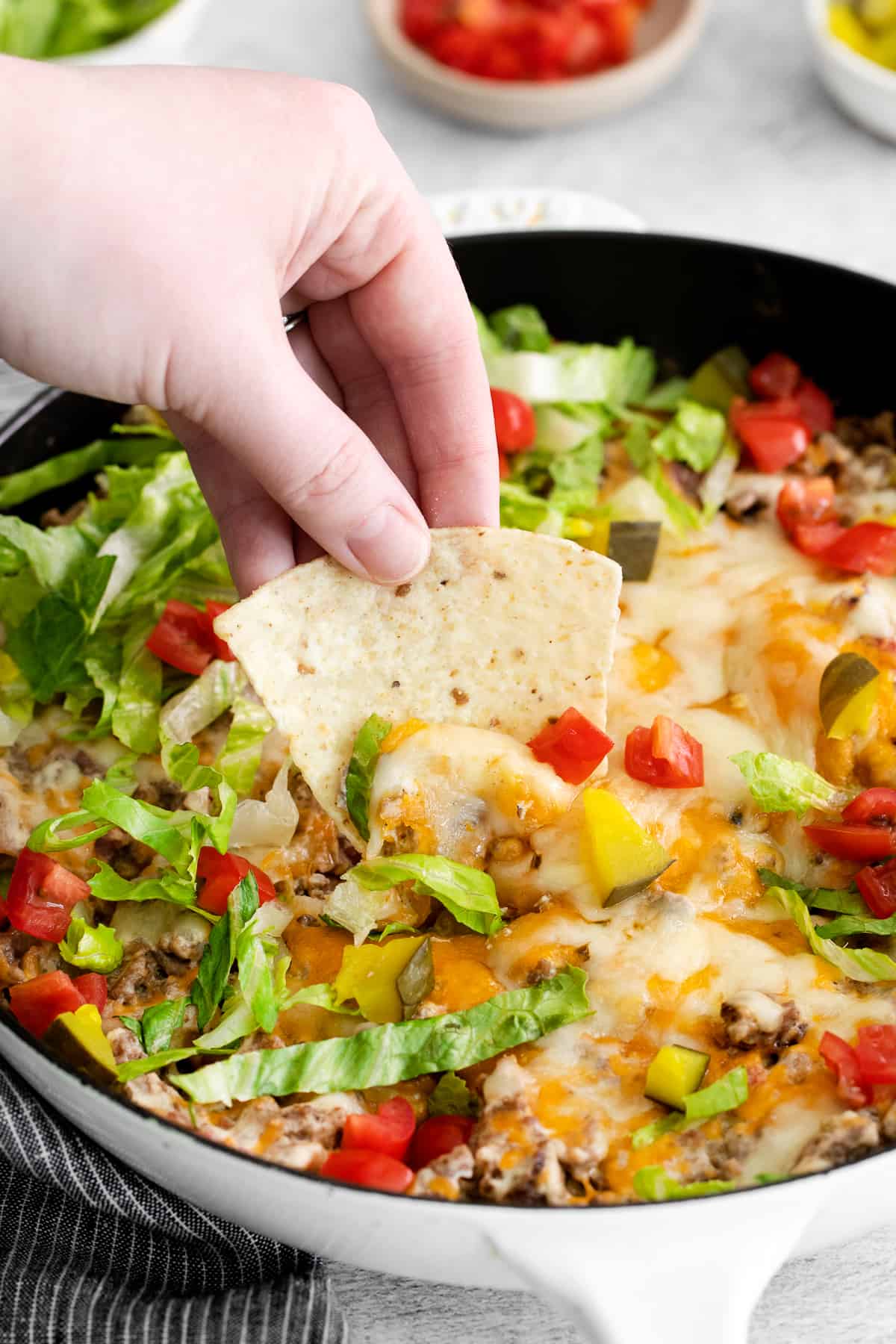 A chip taking a scoop of cheeseburger dip. 