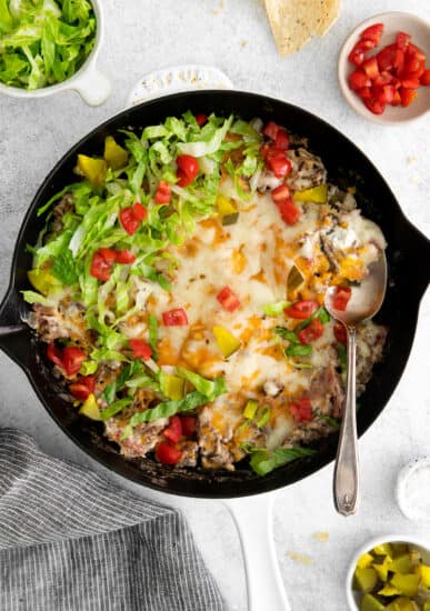 Cheeseburger dip in a skillet with cheeseburger toppings.