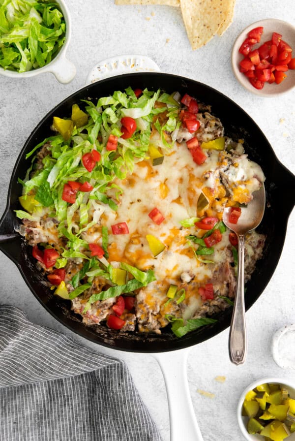 Cheeseburger dip in a skillet with cheeseburger toppings.