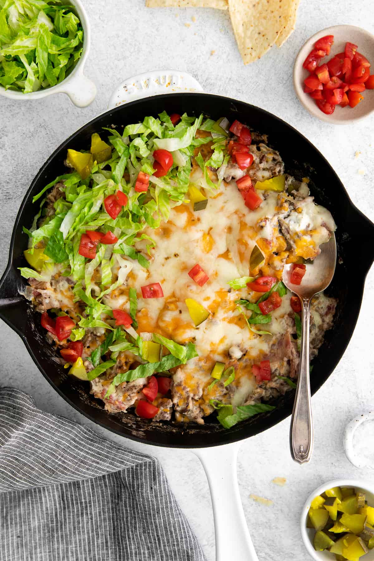 Cheeseburger dip in a skillet with burger toppings. 