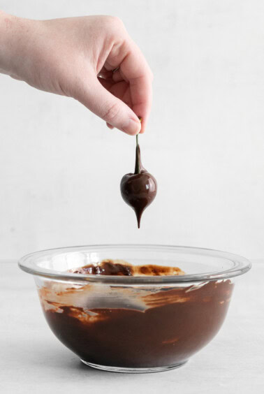 Dipping a cherry into melted chocolate.