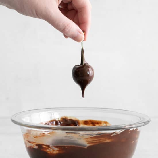 Dipping a cherry into melted chocolate.