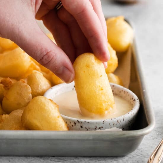 a person dipping a dipping sauce into a tray of french fries.