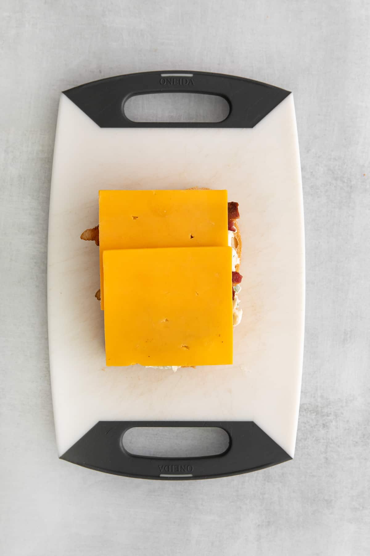 Sliced sharp cheddar cheese on a slice of bread on a cutting board.