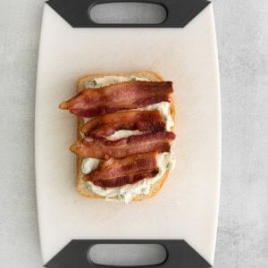 a sandwich with bacon and cheese on a cutting board.