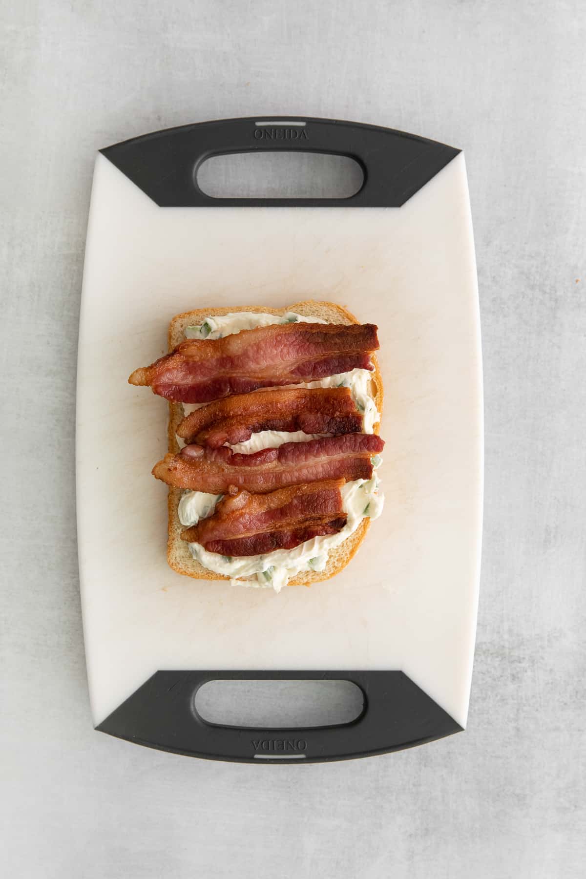 Bacon on top of cream cheese spread on a slice of bread.