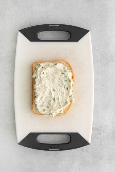 a slice of bread with cream cheese on a cutting board.