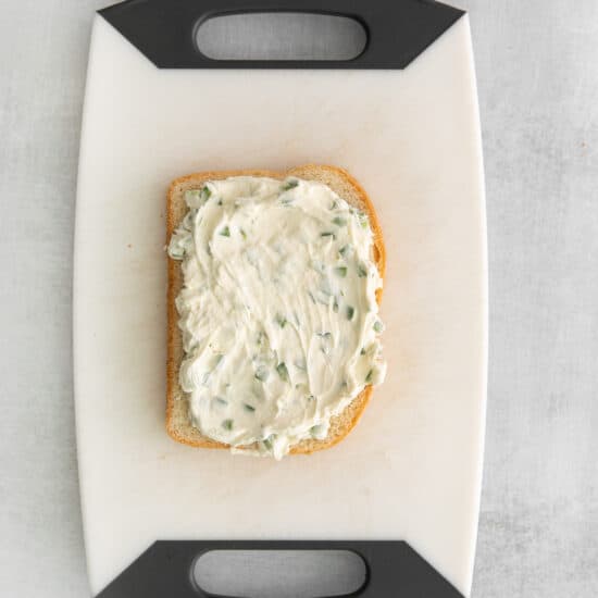 a slice of bread with cream cheese on a cutting board.