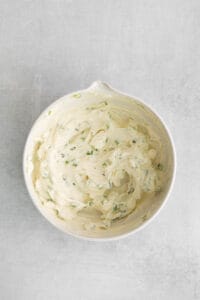 a white bowl of whipped cream with chives on it.