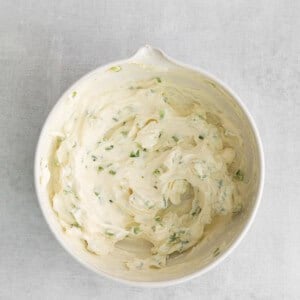 a white bowl of whipped cream with chives on it.