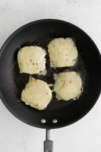 a frying pan with four cheese patties in it.