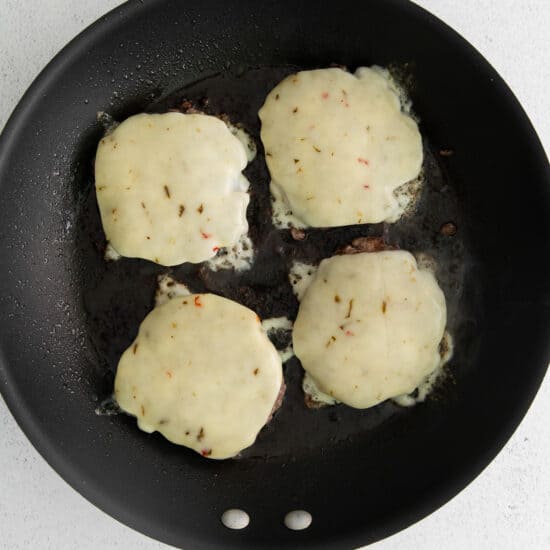 a frying pan with four cheese patties in it.