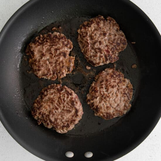 four hamburger patties in a frying pan on a white background.