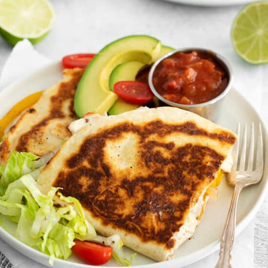 quesadillas on a plate with avocado and tomatoes.