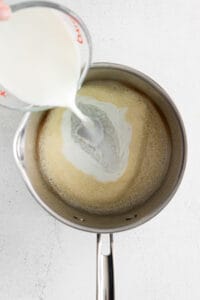 a person pouring milk into a pan.