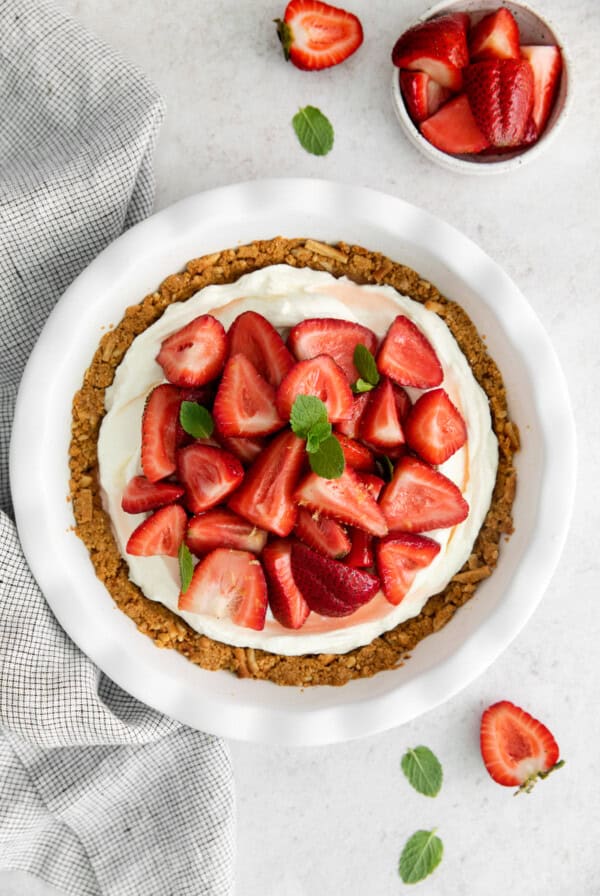 A strawberry cream cheese pie featuring fresh strawberries and a hint of mint, elegantly presented on a white plate.