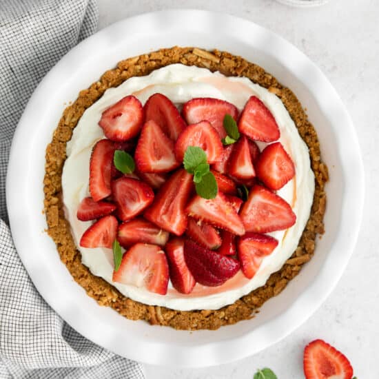 A white plate holds a mouthwatering pie filled with strawberries and cream cheese.