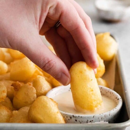 fried cheese curd being dipped into sauce