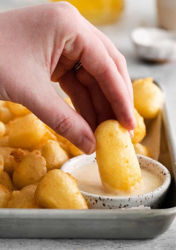 fried cheese curd being dipped into sauce