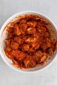a white bowl filled with chicken in a red sauce.