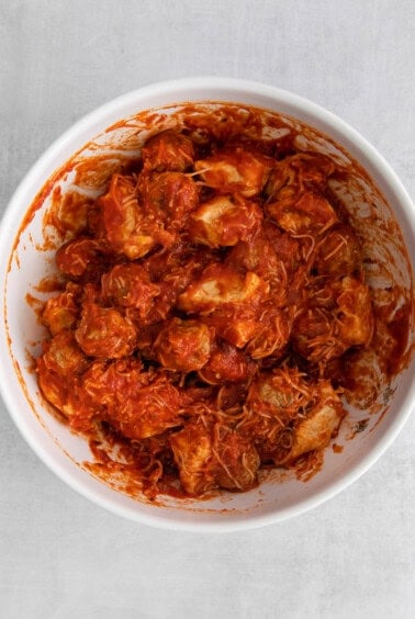a white bowl filled with chicken in a red sauce.