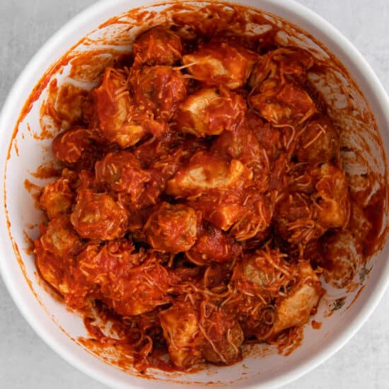 a white bowl filled with chicken in a red sauce.