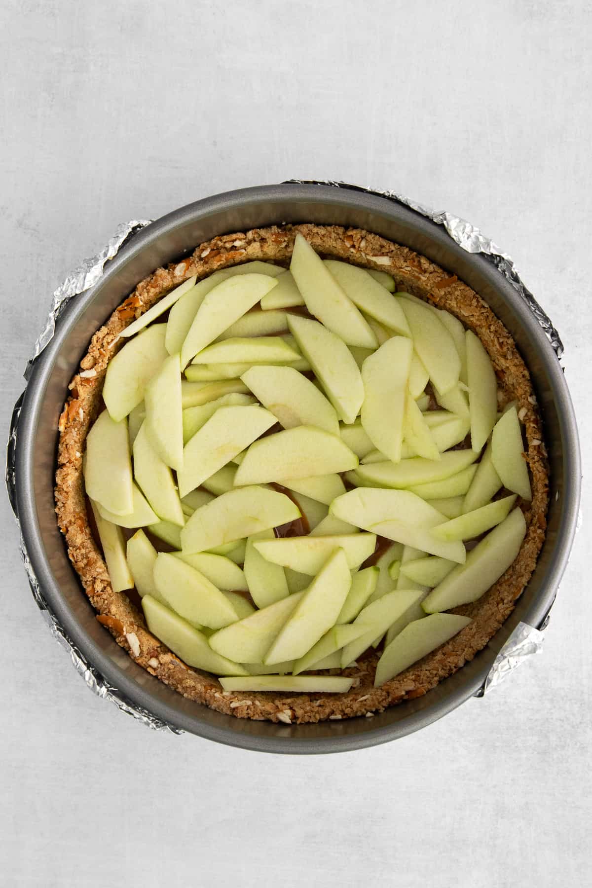 Sliced apples placed over caramel and a cheesecake crust.
