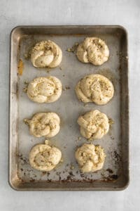 Garlic knots with oil and spices on a baking sheet.