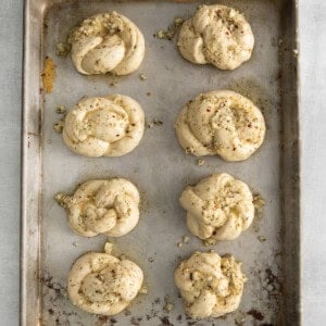 Garlic knots with oil and spices on a baking sheet.