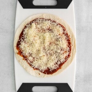 Tortilla topped with sauce and mozzarella cheese.