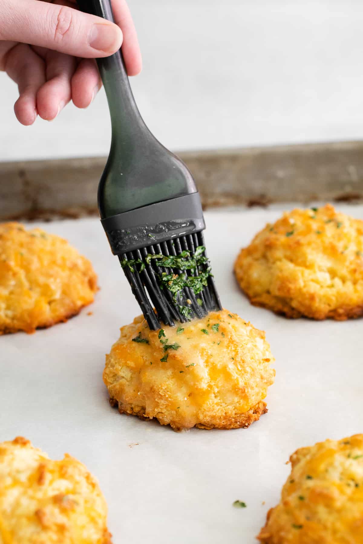Red lobster cheddar biscuit being brushed with butter on a baking sheet.