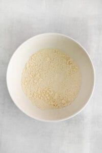 a white bowl of flour on a white surface.