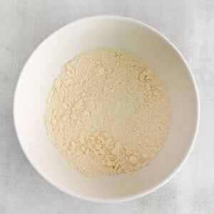 a white bowl of flour on a white surface.