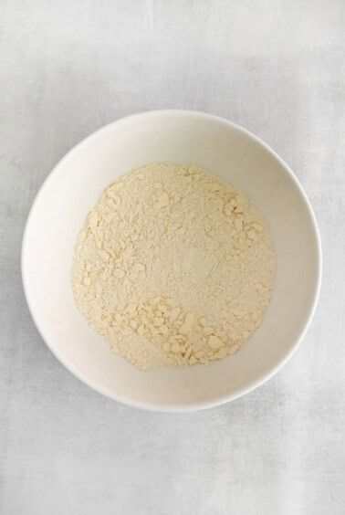 a white bowl of flour on a white surface.