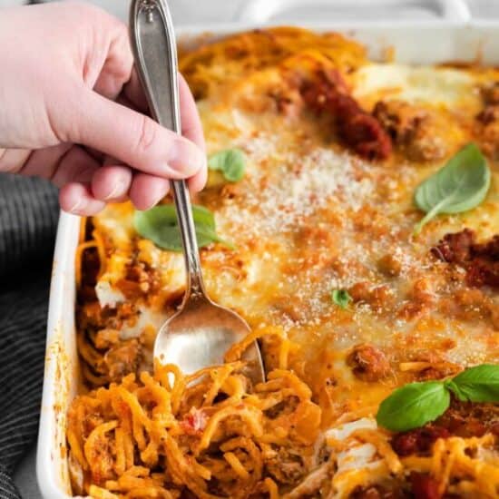 a baking dish and a spoon of baked spaghetti with cream cheese