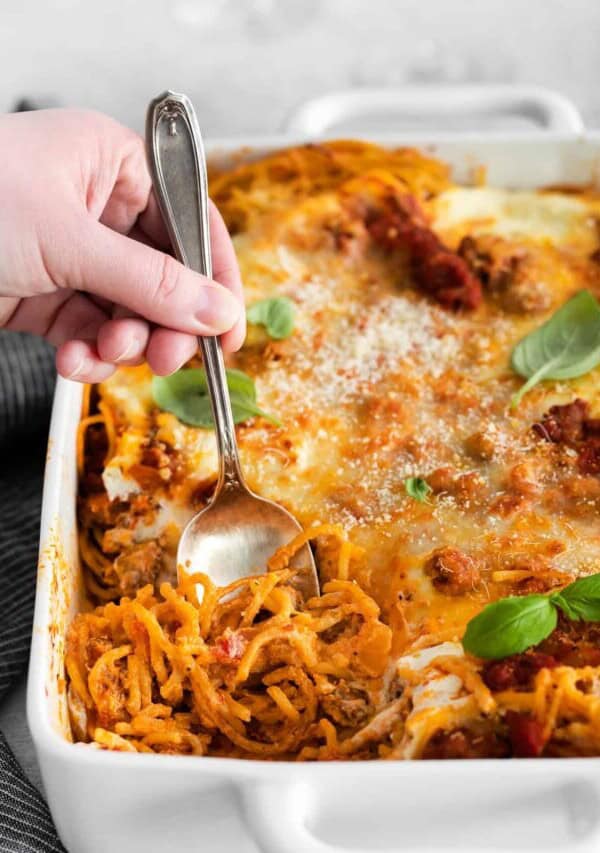 a baking dish and a spoon of baked spaghetti with cream cheese