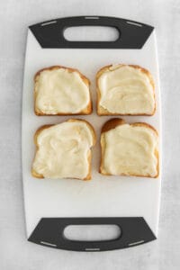 four slices of bread with cream cheese on a cutting board.