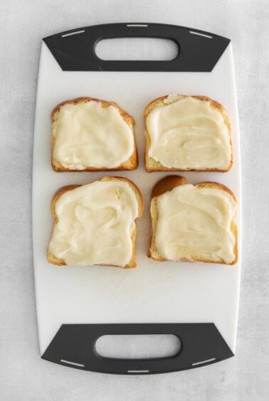 four slices of bread with cream cheese on a cutting board.