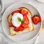 a plate of strawberry toast with whipped cream and strawberries.