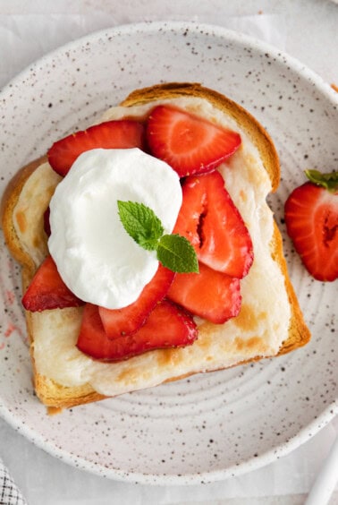 a plate of strawberry toast with whipped cream and strawberries.