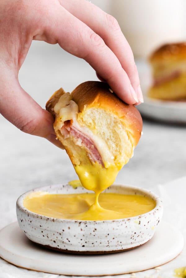 Ham and cheese slider being dipped into a honey mustard sauce.