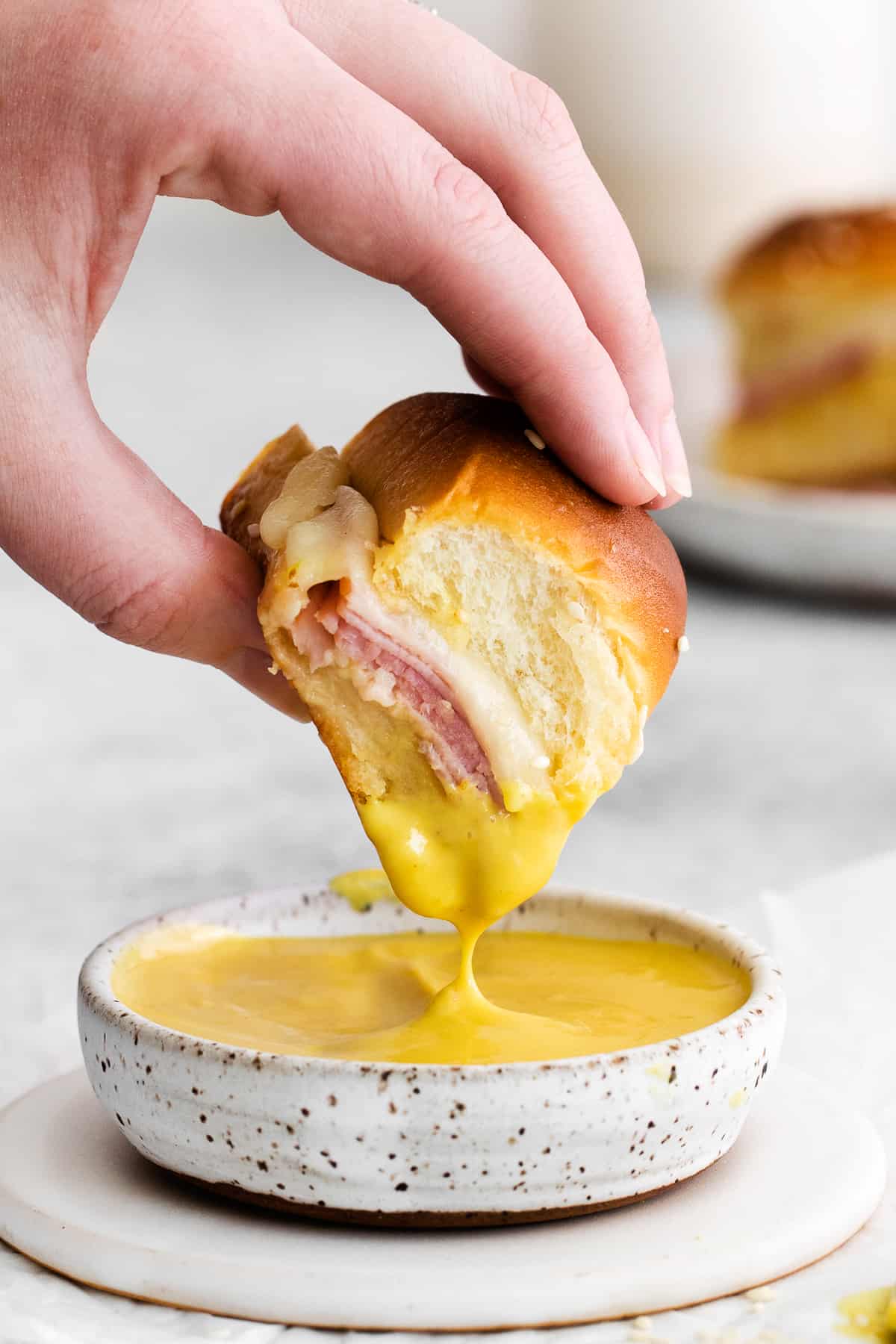 A ham and cheese slider being dipped into honey mustard sauce.