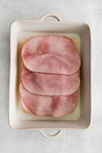 sliced ham in a square dish on a white background.