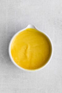 a bowl of yellow sauce on a white surface.