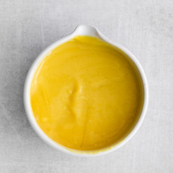 a bowl of yellow sauce on a white surface.