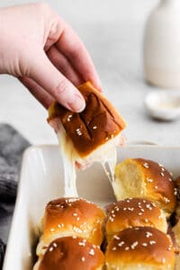 a person dipping ham sliders into a baking dish.