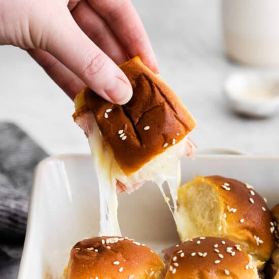a person dipping ham sliders into a baking dish.
